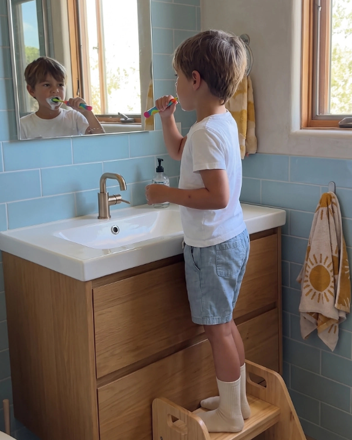 Young child brushing their teeth at the bathroom sink while looking in the mirror