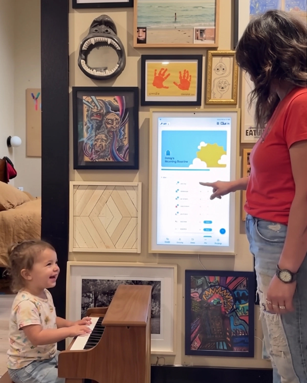 Parent using a wall-mounted digital family planner while a young child plays the piano