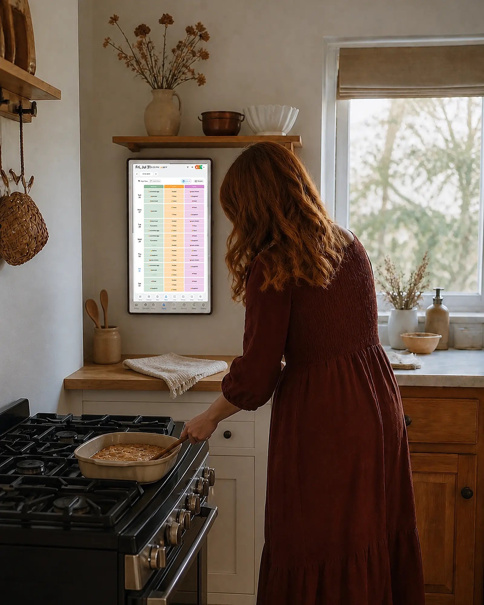 A woman cooks in the kitchen beside a wall-mounted digital family schedule
